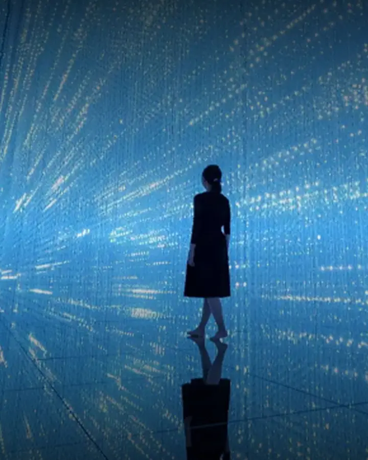 A visitor stands in a blue starfield of light, mirrored in the floor.
