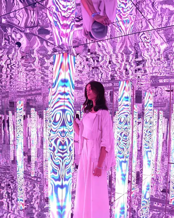 A visitor in a pink dress among mirrored violet pillars.