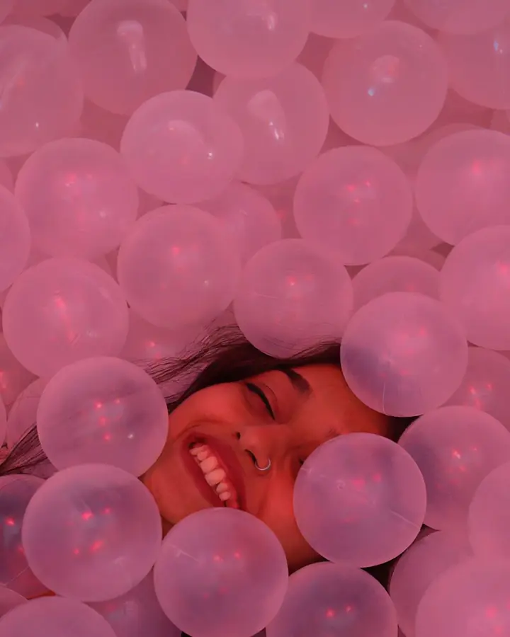 A child laughs, half buried in pink balls.
